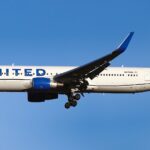 A United Airlines aircraft flying in the blue sky, no clouds, with the landing gear out.