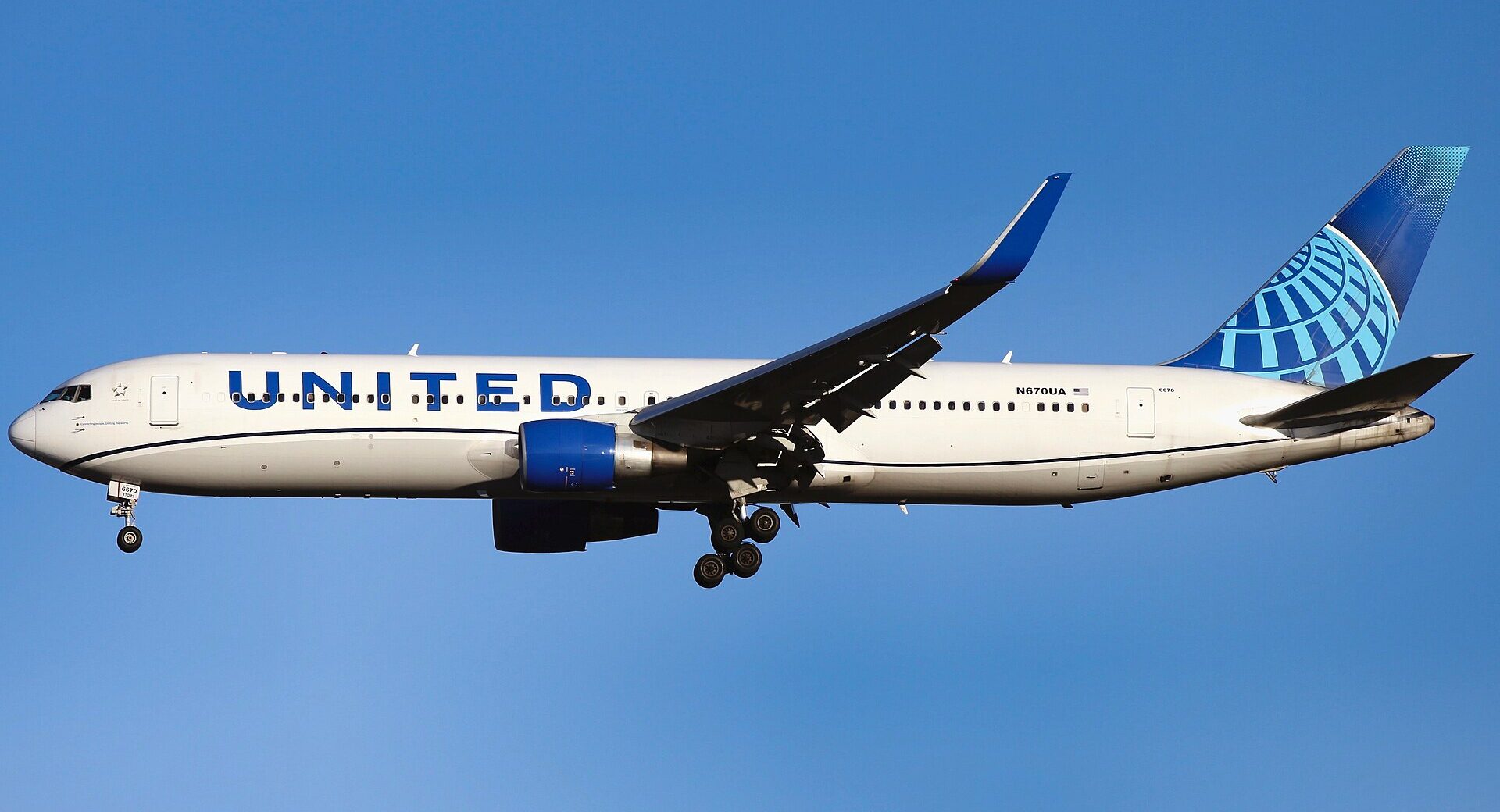 A United Airlines aircraft flying in the blue sky, no clouds, with the landing gear out.