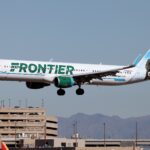 A Frontier Airlines Airbus plane coming in to land at an airport, its landing gear is out. White and green livery.