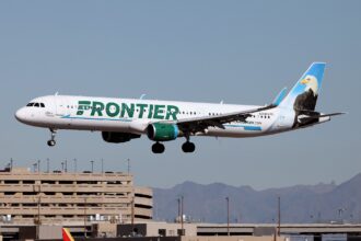 A Frontier Airlines Airbus plane coming in to land at an airport, its landing gear is out. White and green livery.