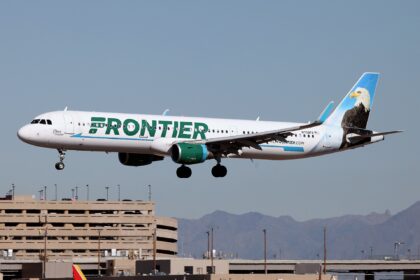 A Frontier Airlines Airbus plane coming in to land at an airport, its landing gear is out. White and green livery.