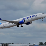 A large blue and white jetliner flying through a cloudy sky