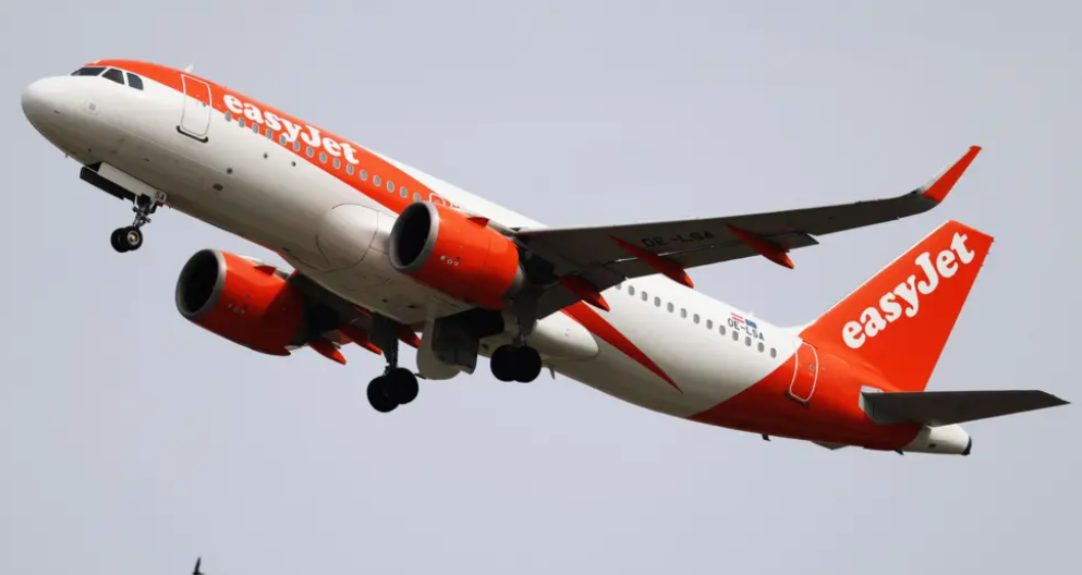 A large orange and white jetliner flying in a grey sky