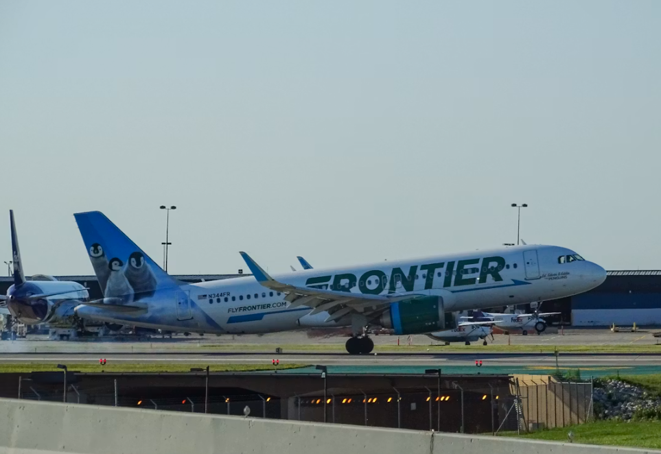 A green and white Frontier jetliner on an airport runway