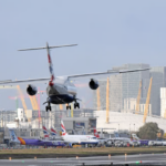 A plane landing at an airport with tall buildings in the background