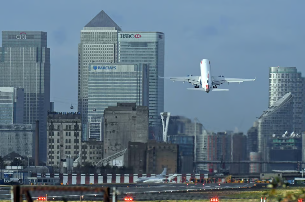 A plane taking off from a runway with tall buildings in the background