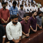 A large group of people standing in rows in a church with their eyes closed and hands clasped.