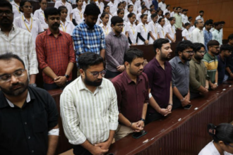 A large group of people standing in rows in a church with their eyes closed and hands clasped.