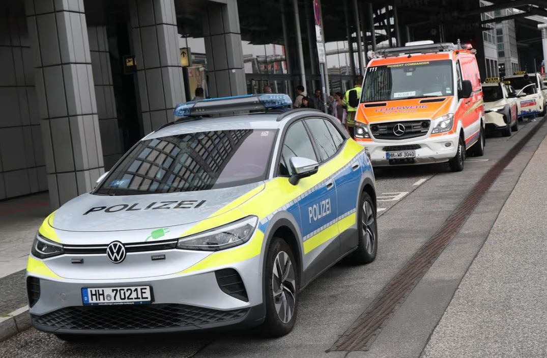 A police car parked outside a grey building, cars parked behind it.