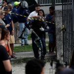 A crowd of people standing beside a concrete wall with caution tape in front of it