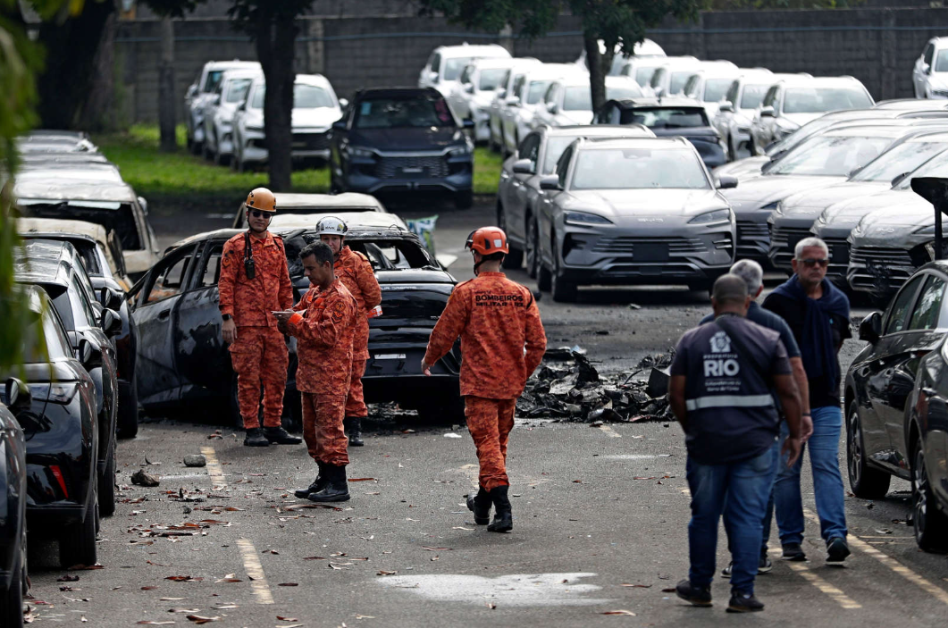 Men gathered in front of a wrecked car, with more cars in the background and trees