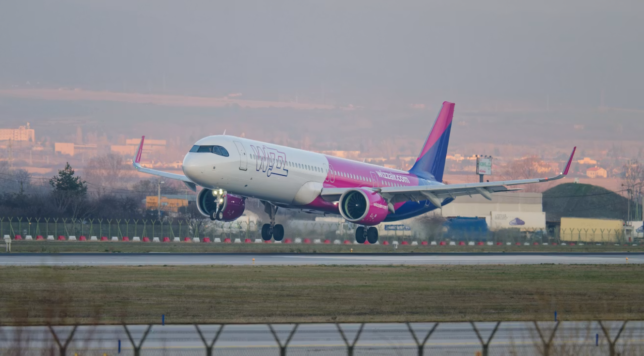 A pink and white plane taking off from an airport runway during the evening