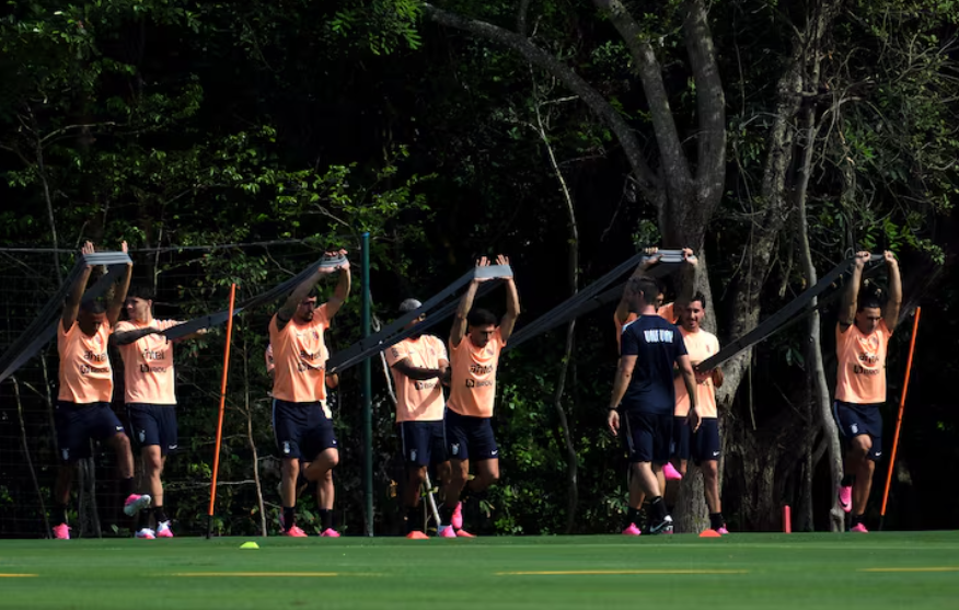A group of men dressed in orange and navy on a sports pitch with trees in the background.