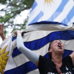 A woman celebrating and holding a blue and white flag, with trees in the background.
