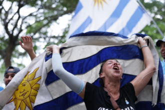 A woman celebrating and holding a blue and white flag, with trees in the background.