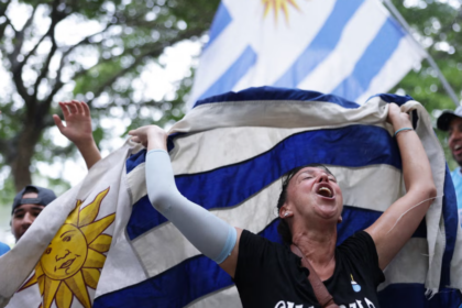 A woman celebrating and holding a blue and white flag, with trees in the background.