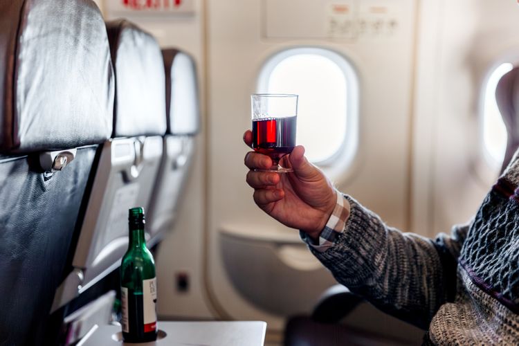 A man holding a glass of red wine on a flight sitting on an isle seat on an aircraft exit row