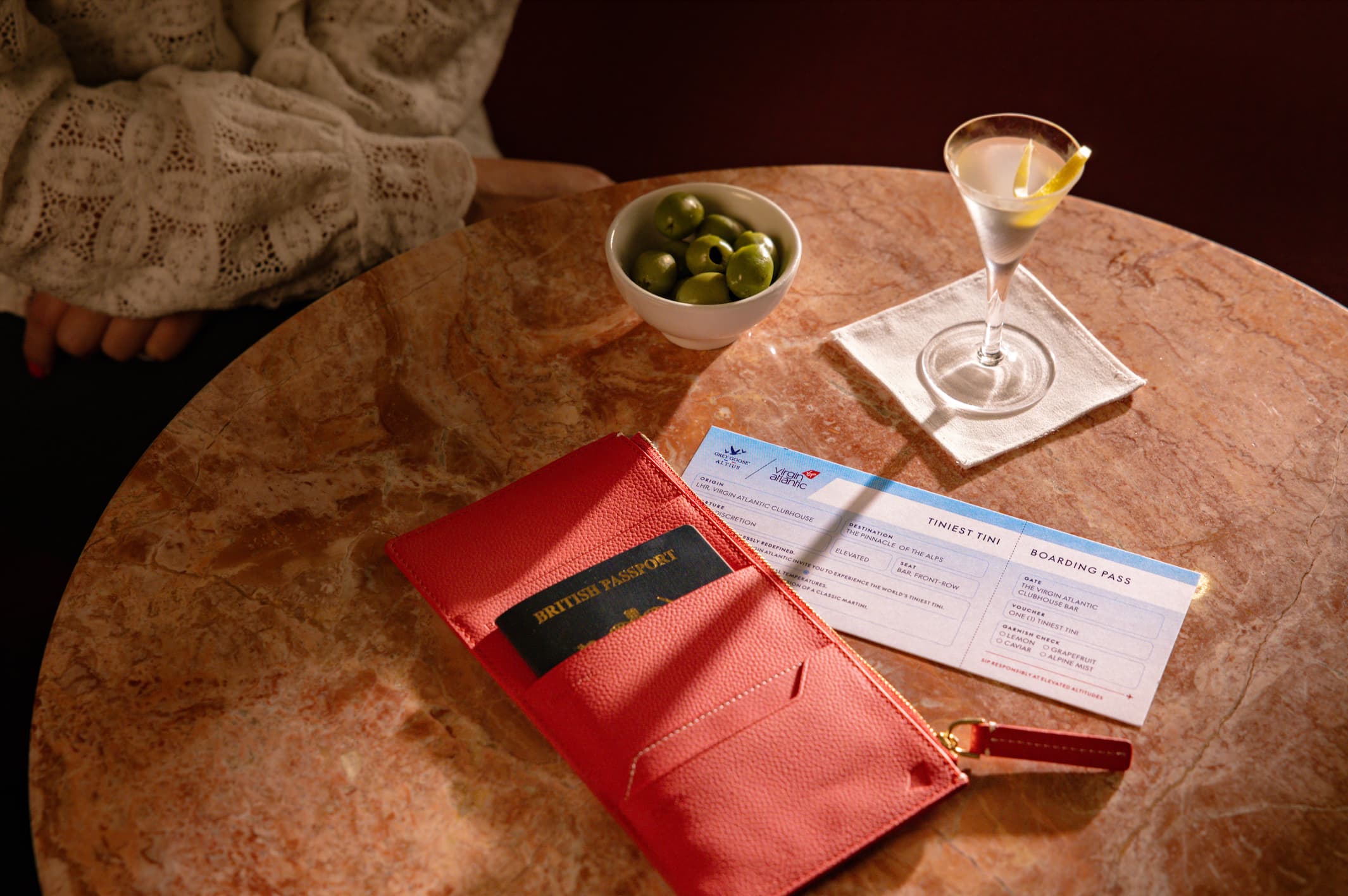 Tiny martini, bowl of olives, passport and special boarding pass arranged on a table with the sunlight coming through.