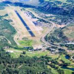 The Aspen/Pitkin County Airport seen from an aerial views. Mountains and trees in view around the base. The runway is seen in the middle.