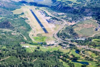 The Aspen/Pitkin County Airport seen from an aerial views. Mountains and trees in view around the base. The runway is seen in the middle.