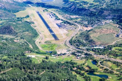 The Aspen/Pitkin County Airport seen from an aerial views. Mountains and trees in view around the base. The runway is seen in the middle.