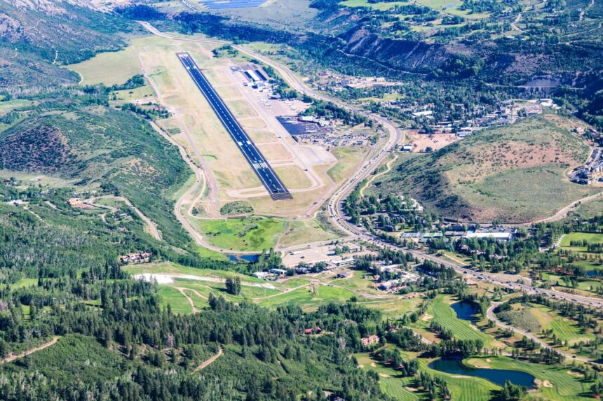 The Aspen/Pitkin County Airport seen from an aerial views. Mountains and trees in view around the base. The runway is seen in the middle.