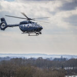 Helicopter flying above trees, under white clouds.