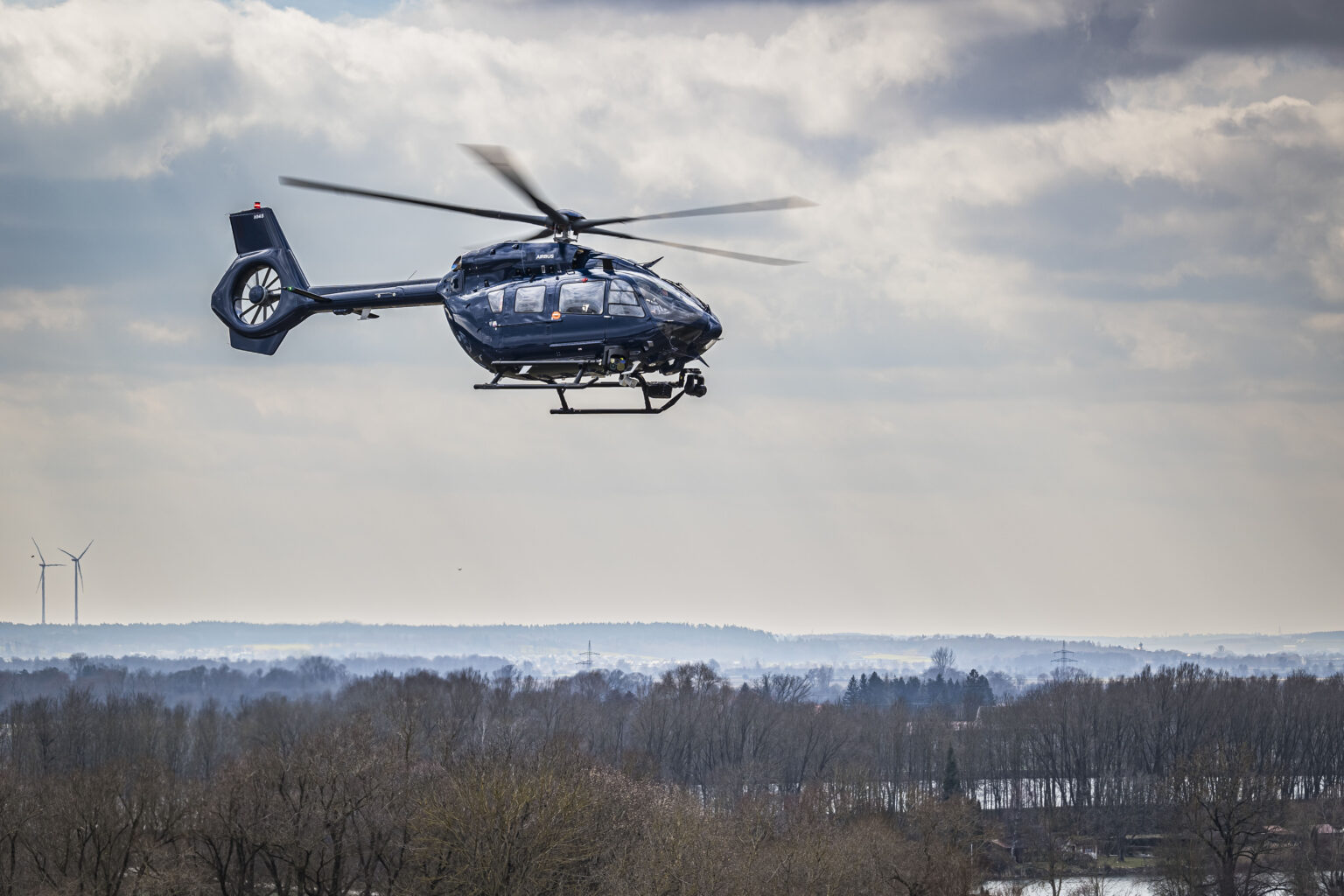 Helicopter flying above trees, under white clouds.