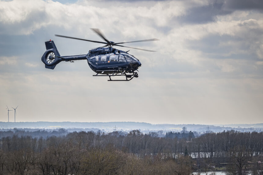 Helicopter flying above trees, under white clouds.