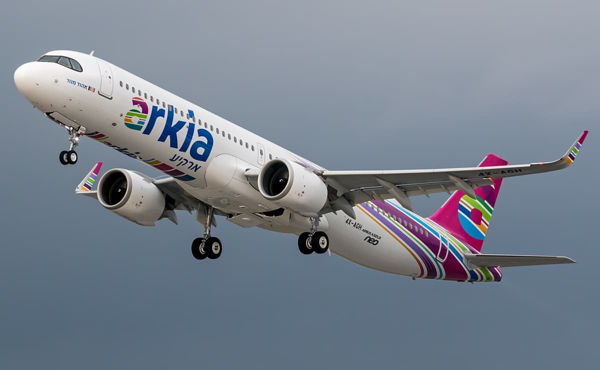 An Arkia Airbus A321neo aircraft flying upwards toward the left side, landing gear still out. Grey sky in the background.