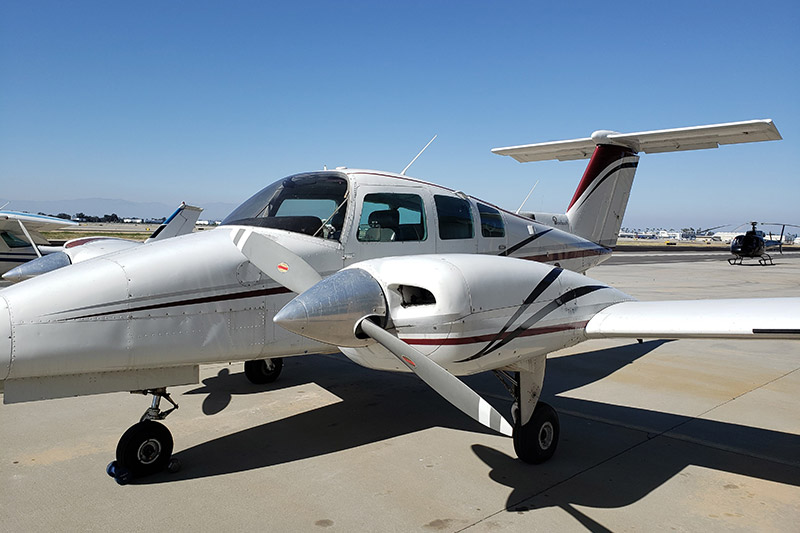 A Beechcraft 76 parked at a runway. The sky is blue and the aircraft's livery is silver with red and black accents.