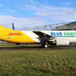 Boeing 737-400SF freighter N901JK in Blue Dart and DHL livery parked on the grass apron near a hangar