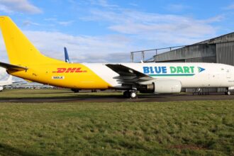Boeing 737-400SF freighter N901JK in Blue Dart and DHL livery parked on the grass apron near a hangar