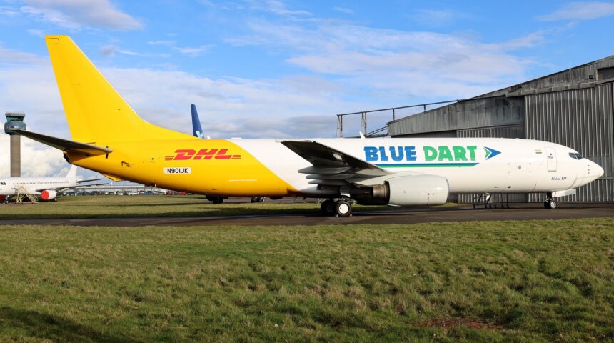 Boeing 737-400SF freighter N901JK in Blue Dart and DHL livery parked on the grass apron near a hangar