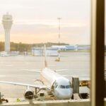 Airport tarmac with an aircraft parked at the gate with ATC tower in the background