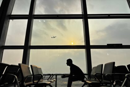 Silhouette of a man sitting at Kolkata Airport with a plane in the sky during sunset.