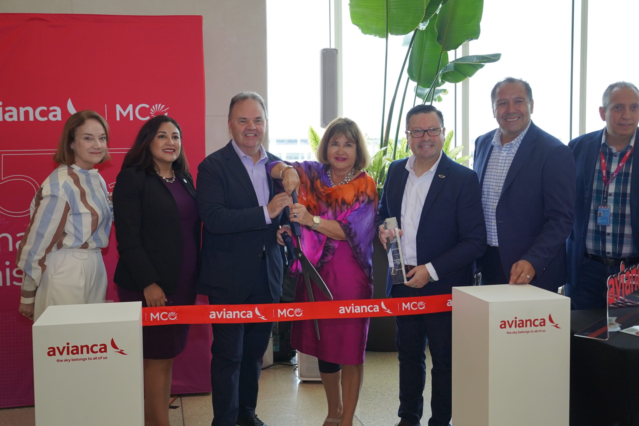 Avianca and MCO officials stand in a line in front of a piece of tape with two people holding large scissors to cut the tape, celebrating 15 years at MCO