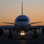 Picture of the front of a plain white Delta Air Lines Boeing 767. The background has a gorgeous blue and orange ombre. There is a warm light glowing off the airplanes nose cone.