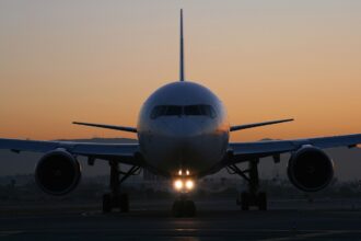 Picture of the front of a plain white Delta Air Lines Boeing 767. The background has a gorgeous blue and orange ombre. There is a warm light glowing off the airplanes nose cone.