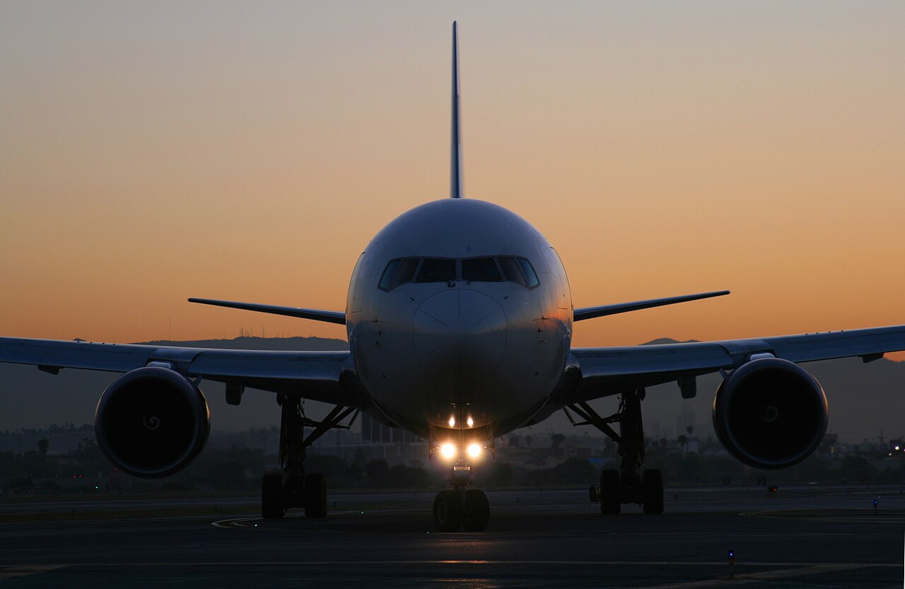 Picture of the front of a plain white Delta Air Lines Boeing 767. The background has a gorgeous blue and orange ombre. There is a warm light glowing off the airplanes nose cone.