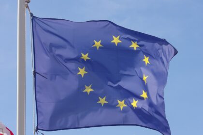 A picture of the dark blue with yellow stars European Union flag fluttering in the wind, with a bright light blue sky in the background.