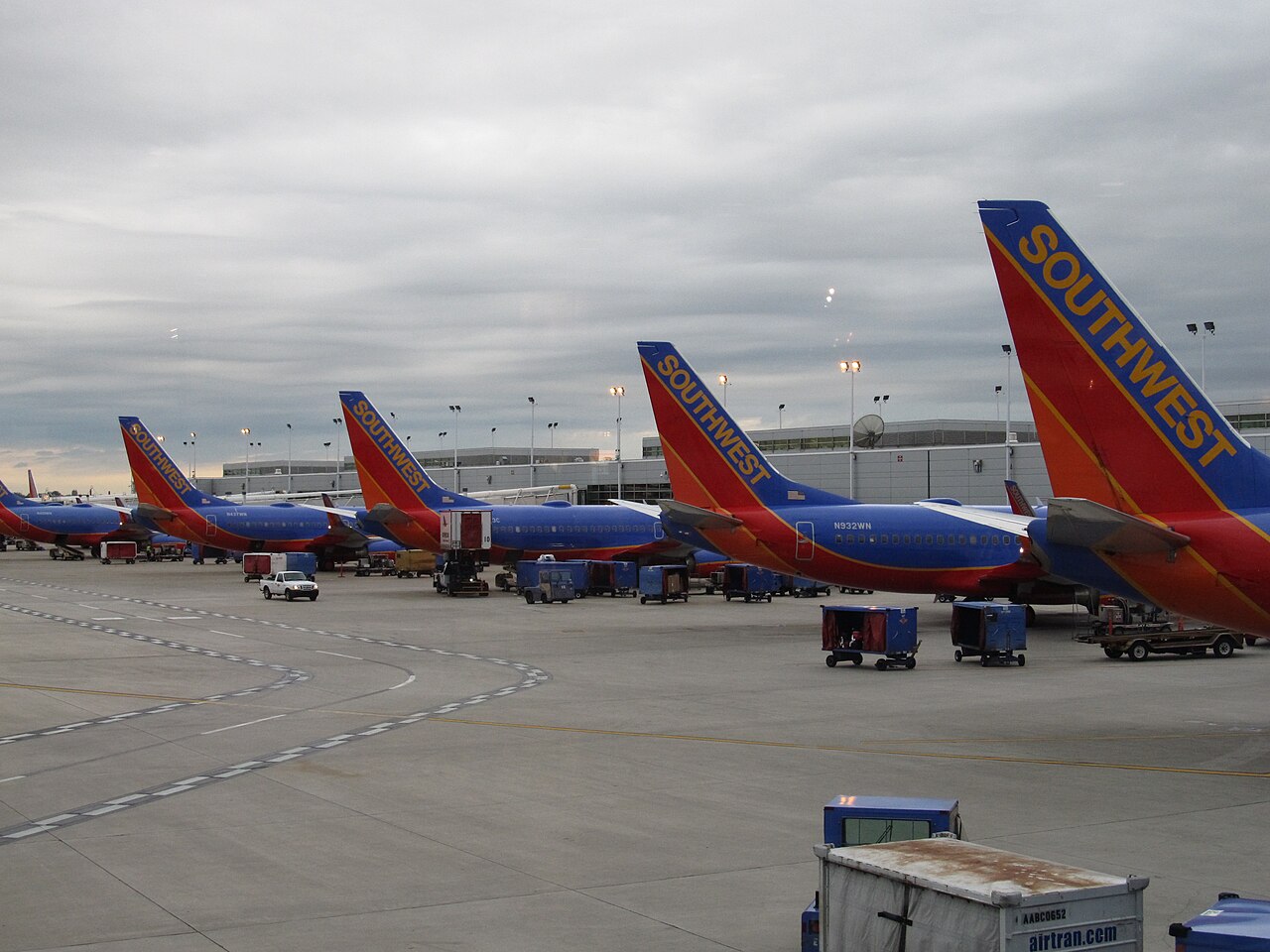 An image of moody and stormy weather at Chicago Midway International Airport. There is a line of bright red and blue Southwest Airplanes. The word 'Southwest' is coloured mustard yellow, along with a thin line separating the red and blue colours decorating the planes body.