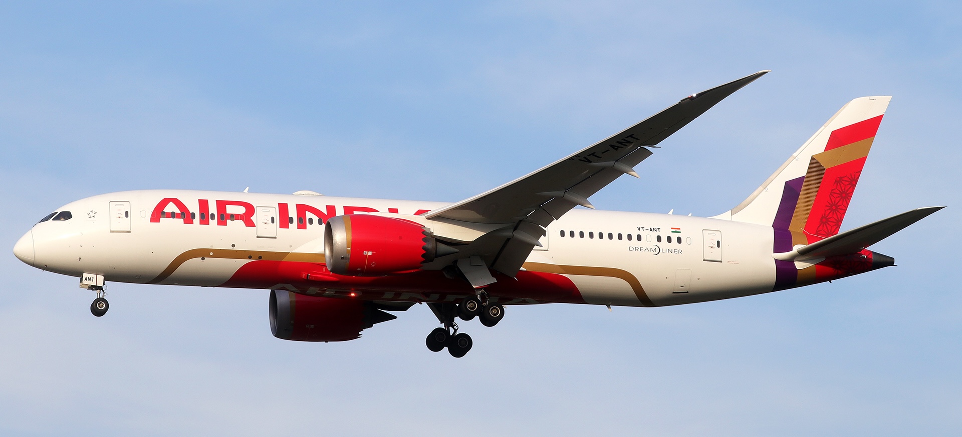 Side view of the full length of an Air India plane with its landing gear extended in the sky.