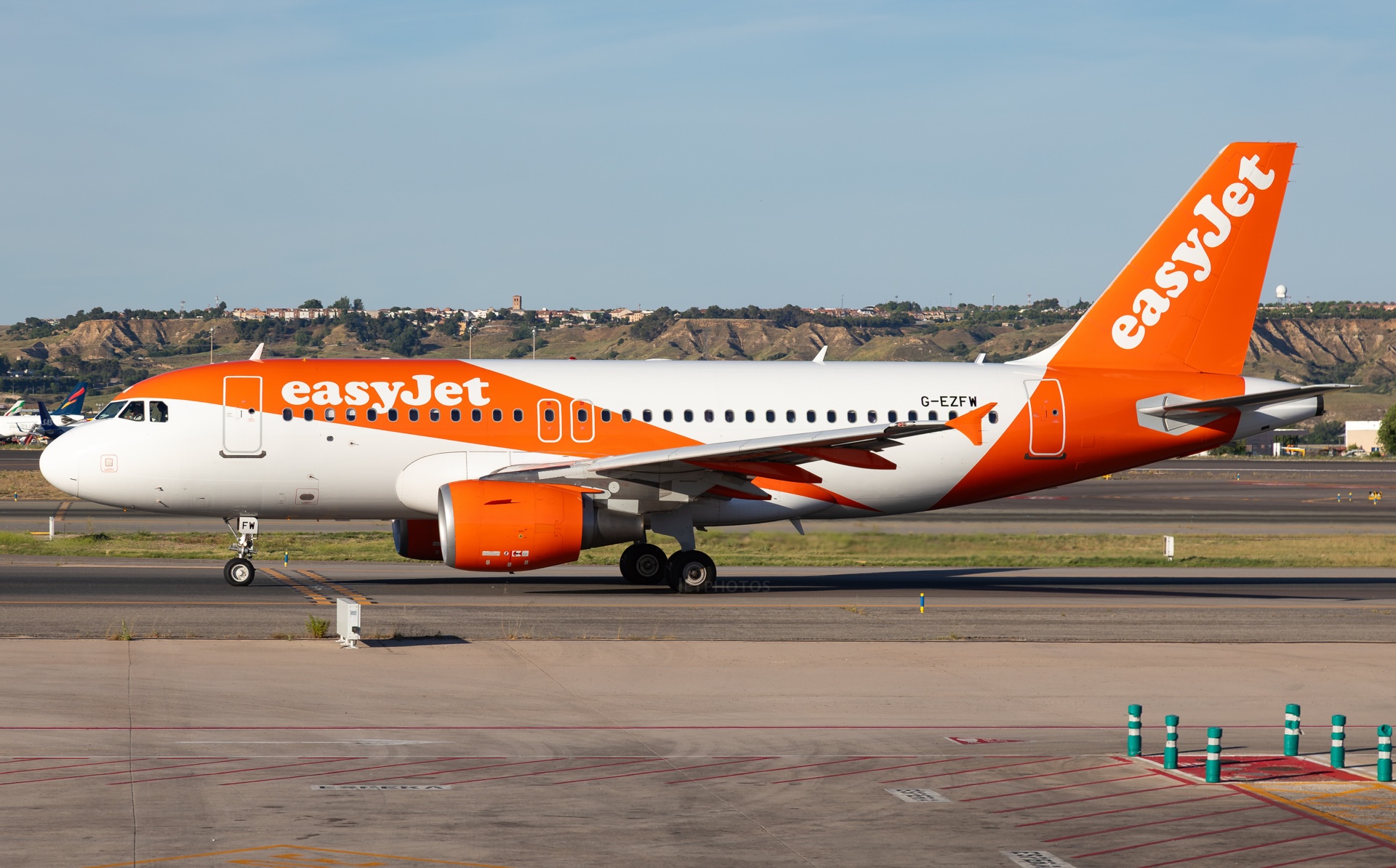 Side view of EasyJet Airbus A319 aircraft in the airline’s orange-and-white on an airport runway.