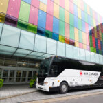 Air Canada branded coach, red and white, parked on a road in front of a colourful building.
