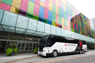 Air Canada branded coach, red and white, parked on a road in front of a colourful building.