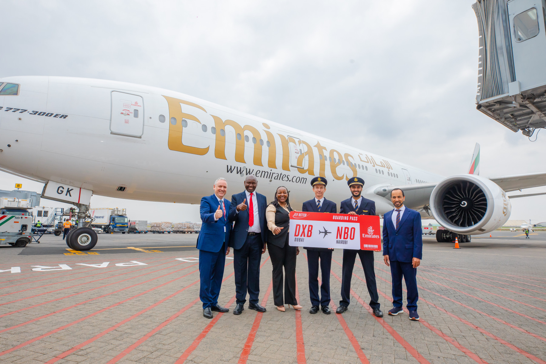 An Emirates aircraft on the runway with 6 people standing in front of it holding a red sign