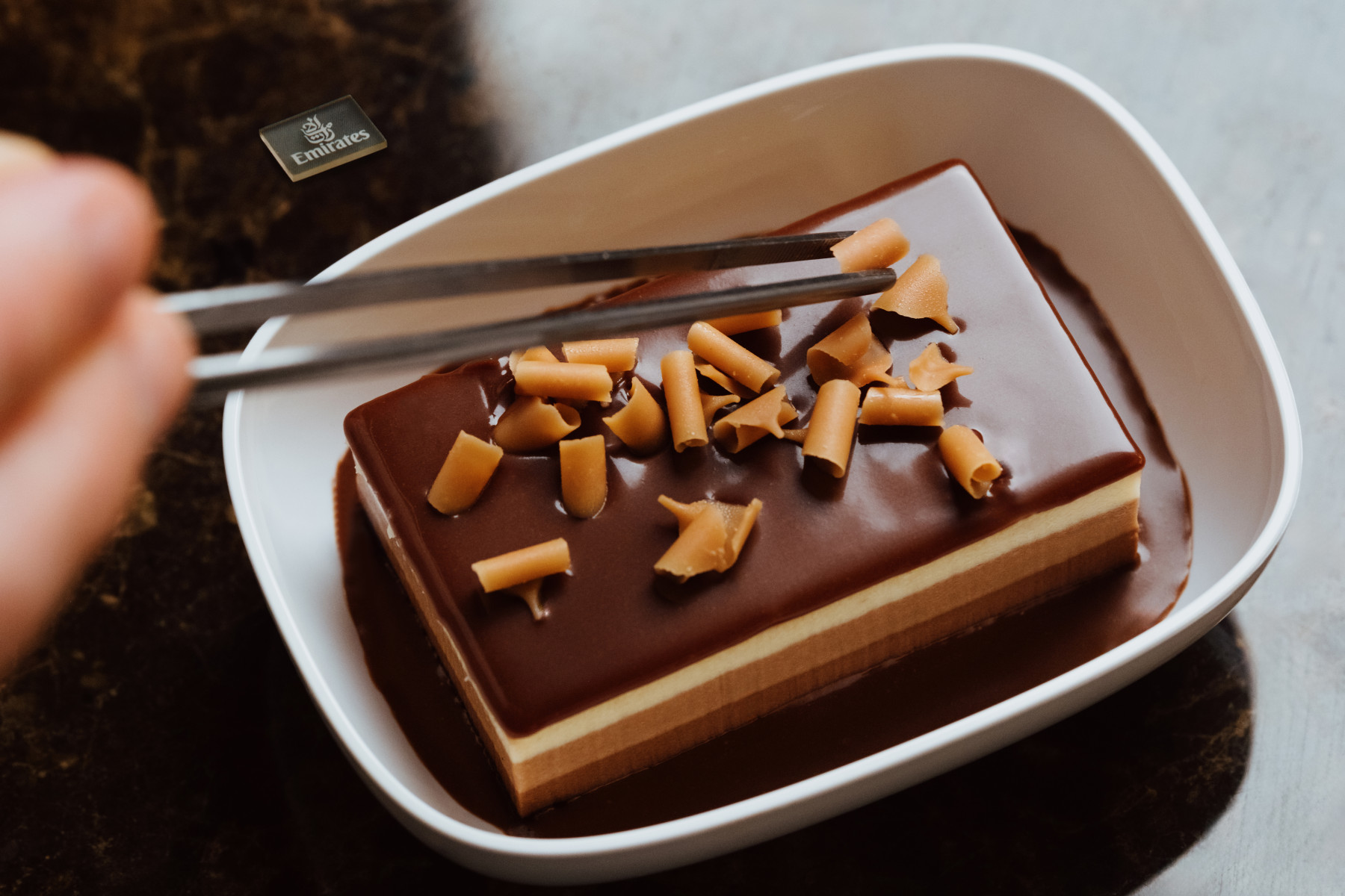 The economy class chocolate mousse dessert being topped with caramel swirls using a tweezer for precision.