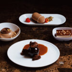 The image shows chocolate desserts curated by Emirates, across all classes of travel. Economy customers may enjoy Emirates’ Triple Chocolate Mousse Cake with chocolate sauce and caramel curls. Premium Economy customers may indulge in Emirates’ Chocolate & Pistachio Mousse Cake with apricot curd. Business class customers are treated to Emirates’ Chocolate Entremet with cocoa glaze, dark chocolate soil and gold raspberry. First class customers are offered Emirates’ decadent Chocolate Cake with sponge, dulcey soil and chocolate hazelnut sauce.