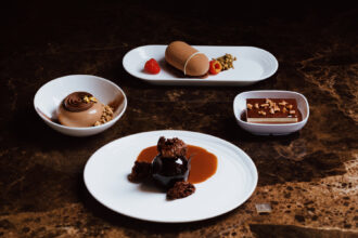 The image shows chocolate desserts curated by Emirates, across all classes of travel. Economy customers may enjoy Emirates’ Triple Chocolate Mousse Cake with chocolate sauce and caramel curls. Premium Economy customers may indulge in Emirates’ Chocolate & Pistachio Mousse Cake with apricot curd. Business class customers are treated to Emirates’ Chocolate Entremet with cocoa glaze, dark chocolate soil and gold raspberry. First class customers are offered Emirates’ decadent Chocolate Cake with sponge, dulcey soil and chocolate hazelnut sauce.